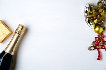 New Year's red and golden decorations, present, bottle of champagne on white wooden background with copy space.