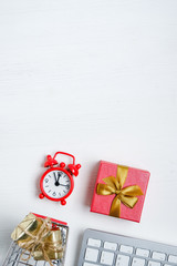 Christmas online shopping concept. White keyboard with red clock, trolley and gift on a wooden background.