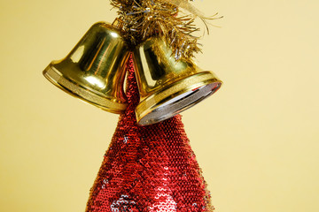 Bottle of champagne with red sparkles and golden Christmas bells on a background of yellow whatman.