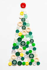 Creative image of handmade Christmas tree made of colorful round sewing buttons in green, beige, yellow, white, red colors isolated on white background. New Year concept. Flat lay. 