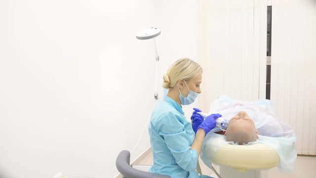microneedle RF lifting procedure. Hardware cosmetology. Beautician conducts a facial rejuvenation procedure for a bald woman.