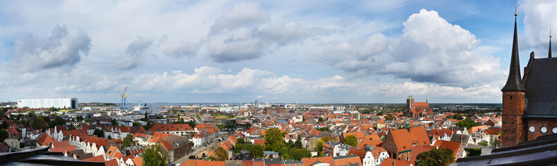 Fototapeta na wymiar panorama cityscape of the old town of wismar, aerial high angle view from the shipyards at the baltic sea to the harbor over the roofs to the st. georgen church, sky with clouds, copy space