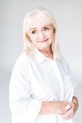 dreamy blonde senior woman in white clothes looking away isolated on grey