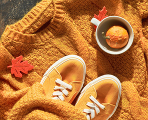 Autumn flat lay with yellow sweater, decorative pumpkin in tea cup and autumn leaves