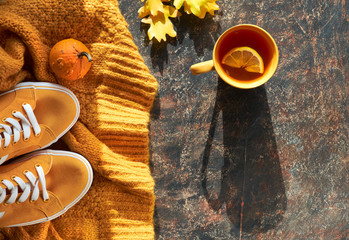 Autumn flat lay with yellow sweater, sneakers, decorative pumpkins, oak leaves and cup of tea with lemon on dark