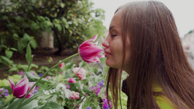 Rainy day. Beautiful woman sniffing pink tulip with water drops on the city flowerbed