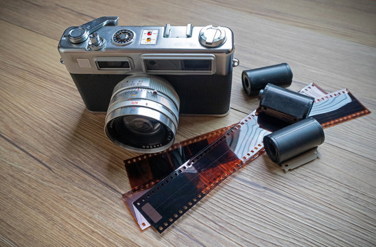 Rangefinder film camera with 35mm film rolls on wooden table.
