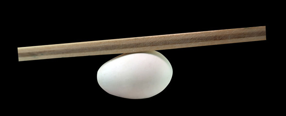 Balance concept, board on egg balance isolated on the black background, balancing on seesaw in...