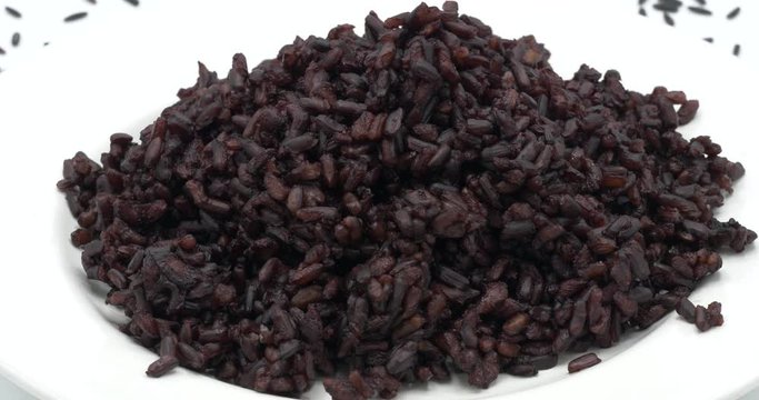 Steamed Riceberry rice on plate rotating on white background, organic rice from Thailand.