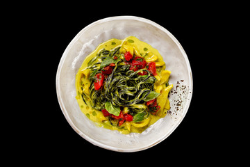 Top view plate of black spaghetti with squid and tomatoes served with sauce isolated at black background.