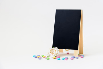 Blank black chalkboard easel with pastel-colored hard-shelled candies on a white background
