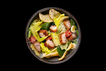 Top view image of caesar salad served in an iron pan isolated at black background. - obrazy, fototapety, plakaty