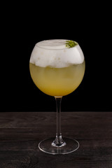 Closeup glass of sour cocktail with egg foam at wooden table isolated at black background.