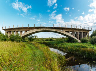 Big old abandoned bridge over small river.
