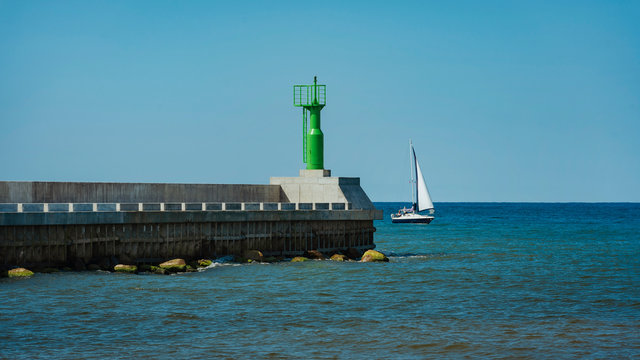 Modern lighthouse pole in green and boat entering sea gates in baltic sea, Pavilosta.