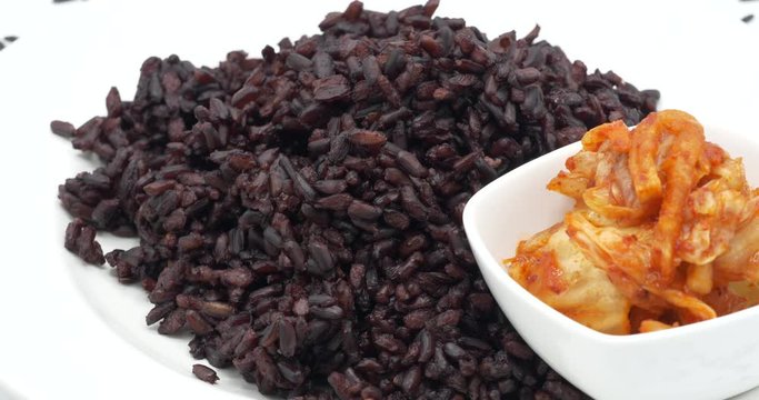 Steamed Riceberry rice on plate with For cabbage kimchi rotating on white background, organic   rice from Thailand.