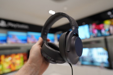 Obraz na płótnie Canvas Gray headphones in a male hand in an electronics store. TVs in the background.