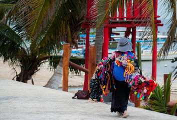 Street vendor woman selling colorful traditional handmade souvenirs near the beach at Puerto Morelos, Mexico