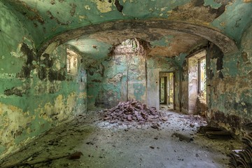 Innenaufnahme eines verlassenen Gebäudes mit grünen Wänden und eingestürzter Decke