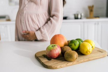cropped view of pregnant woman touching belly near fruits on table