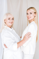 smiling blonde grandmother and granddaughter embracing in total white outfits