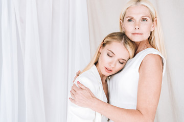 beautiful elegant blonde mother and daughter embracing on white background