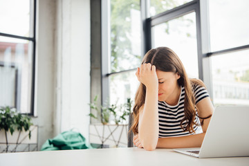 sad girl in striped t-shirt using laptop at home