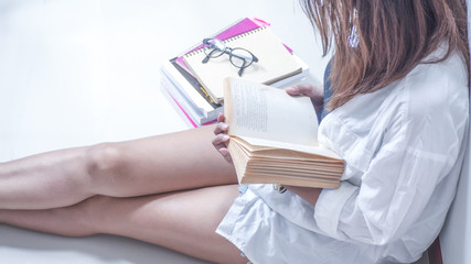 Women wearing white shirts, shorts  , Sitting on a white chair reading a book. And there are stacks of books nearby. Concept  Education,  love to read.