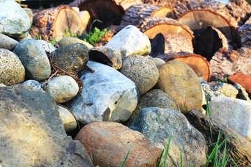 Pile of colorful rocks with cut firewood log rounds behind on a sunny morning