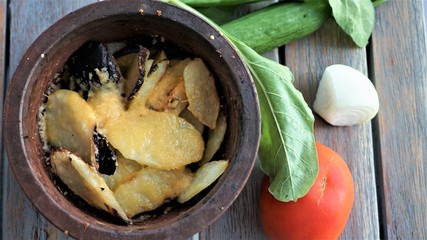 roasted potato in pottery and green salad at wooden surface