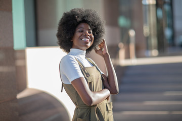Beautiful African American girl with a smile and curly hair, fashionable overalls, and white turtleneck.