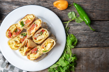 Mexican egg burritos with fresh sauce on wooden background