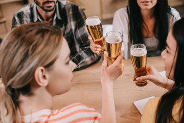 cropped view of multicultural friends clinking glasses of light beer in pub