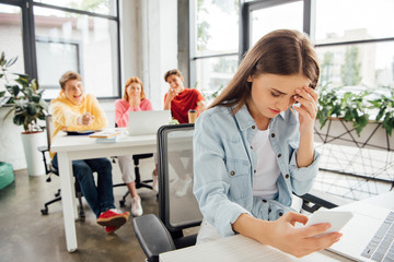 laughing schoolchildren bullying sad girl with smartphone in school