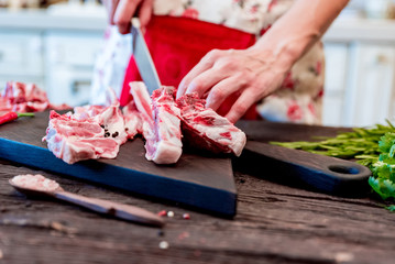 Cook chops raw lamb ribs on kitchen table close up