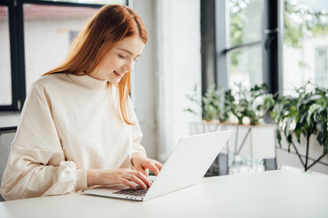 smiling attractive girl sitting at table and using laptop at home