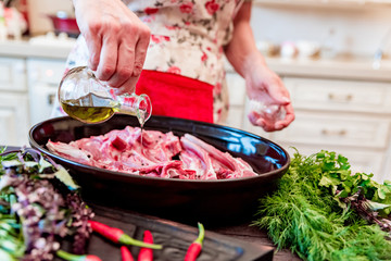 Cook adds oil to raw lamb ribs on frying pan close up