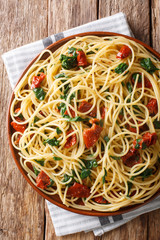 Italian tasty spaghetti with sun-dried tomatoes and spinach close-up on a plate. Vertical top view