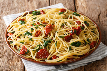Serving of spaghetti with dried tomatoes, cheese and spinach close-up on a plate. horizontal