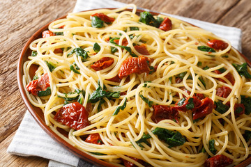 Side dish of spaghetti with dried tomatoes, cheese and spinach close-up on a plate. horizontal