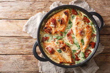 Main course baked chicken with sun-dried tomatoes and spinach in cheese sauce close-up in a pan....