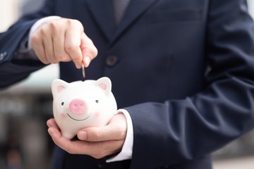businessman putting coin into piggy bank