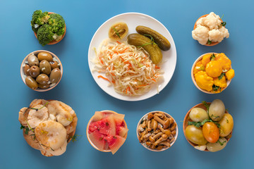 Fermented products cabbage, peppers, pickles, tomatoes, mushrooms, zucchini, garlic on a blue table. Top view