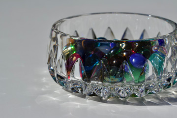 Closeup view of a modern style lead crystal bowl containing colorful glass dragon tears pebbles, with white background