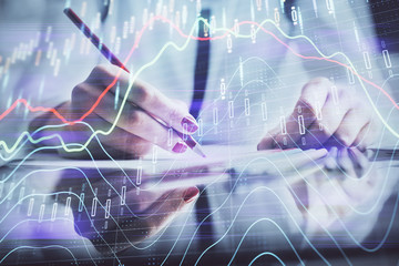 A woman hands writing information about stock market in notepad. Forex chart holograms in front. Concept of research.