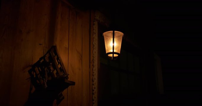 Iron lantern swaying in wind, night light, shadows on wooden wall of rustic barn