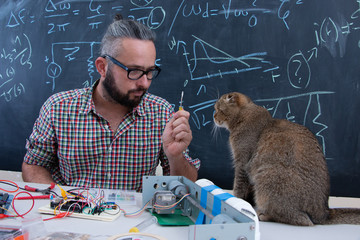 Hipster guy working on arduino project getting visited by cute Scottish fold cat