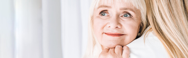 panoramic shot of blonde smiling grandmother gently embracing granddaughter