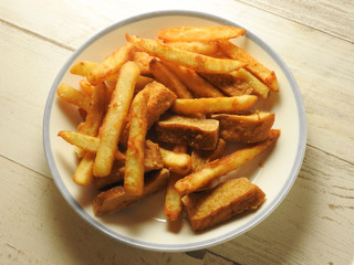 Top view of a plate of French fries and dried tofu on wooden background. Fried food concept. High calories.