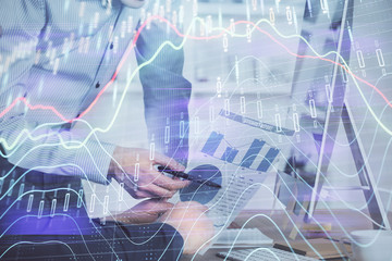 Double exposure of chart with businessman typing on computer in office on background. Concept of hard work.